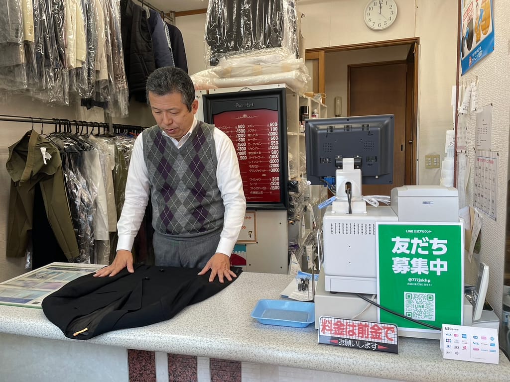 新生クリーニング 受付風景 衣類を丁寧に確認する店主 練馬区