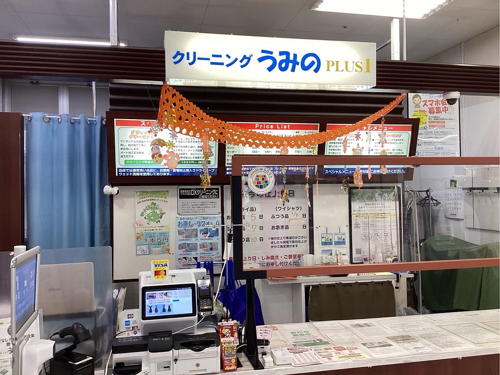 クリーニングうみのPLUS1店の受付カウンター。料金案内やサービス説明が掲示された店内の様子