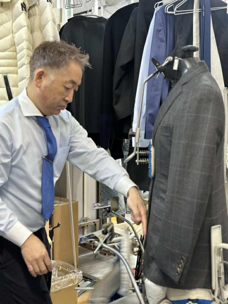 クリーニング作業中の様子。店主がジャケットの形を整えながら丁寧に仕上げを行っている場面。