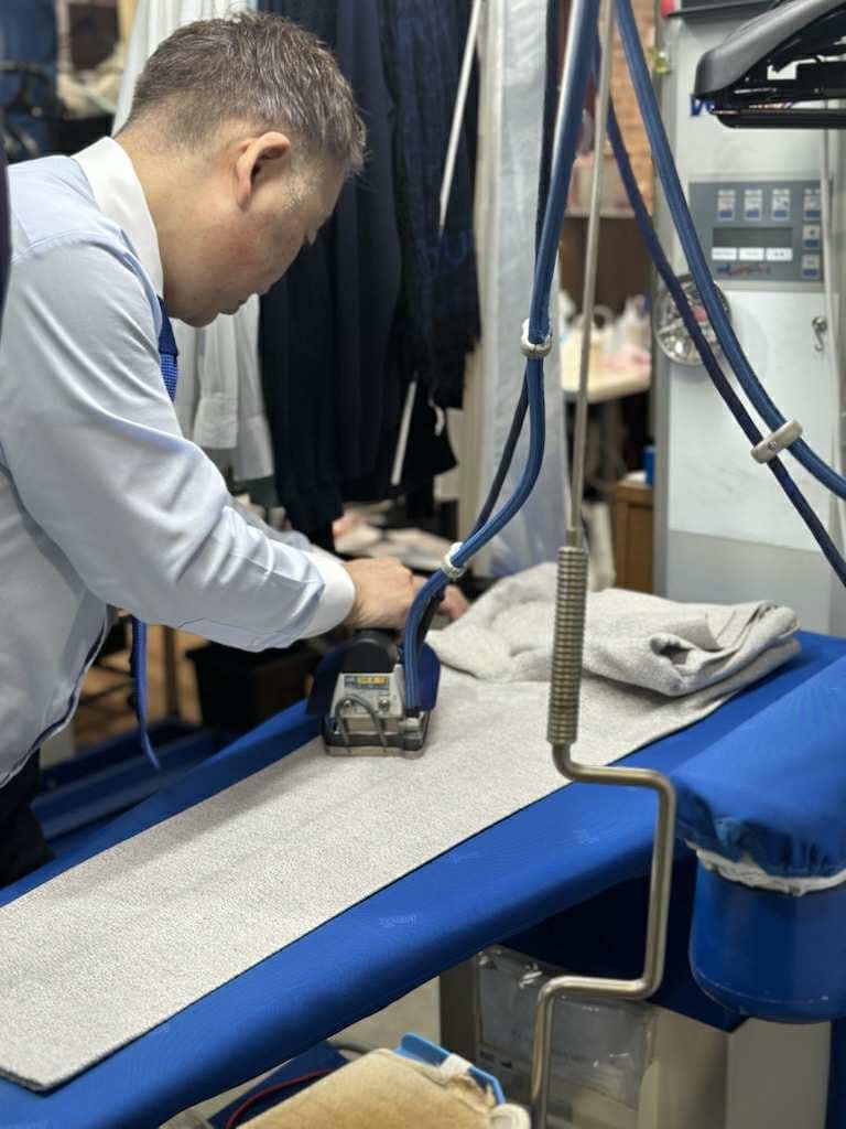 細部まで整えるため、店主が手作業で丁寧にアイロン仕上げを行っているクリーニング工程。