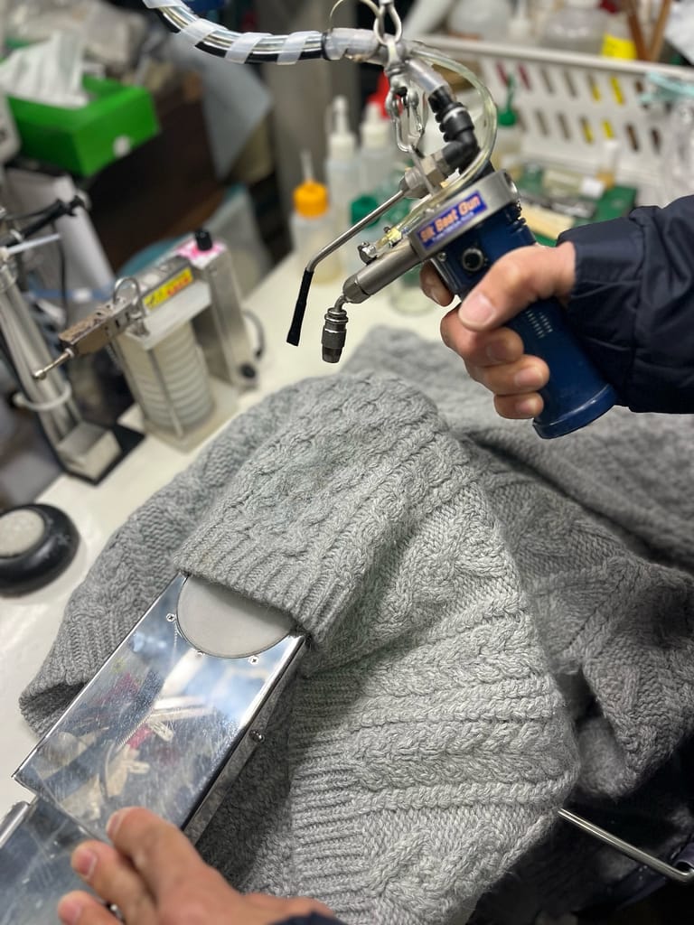 松野クリーニング本店で専用機器を使ってニットのシミ抜きを行う作業風景