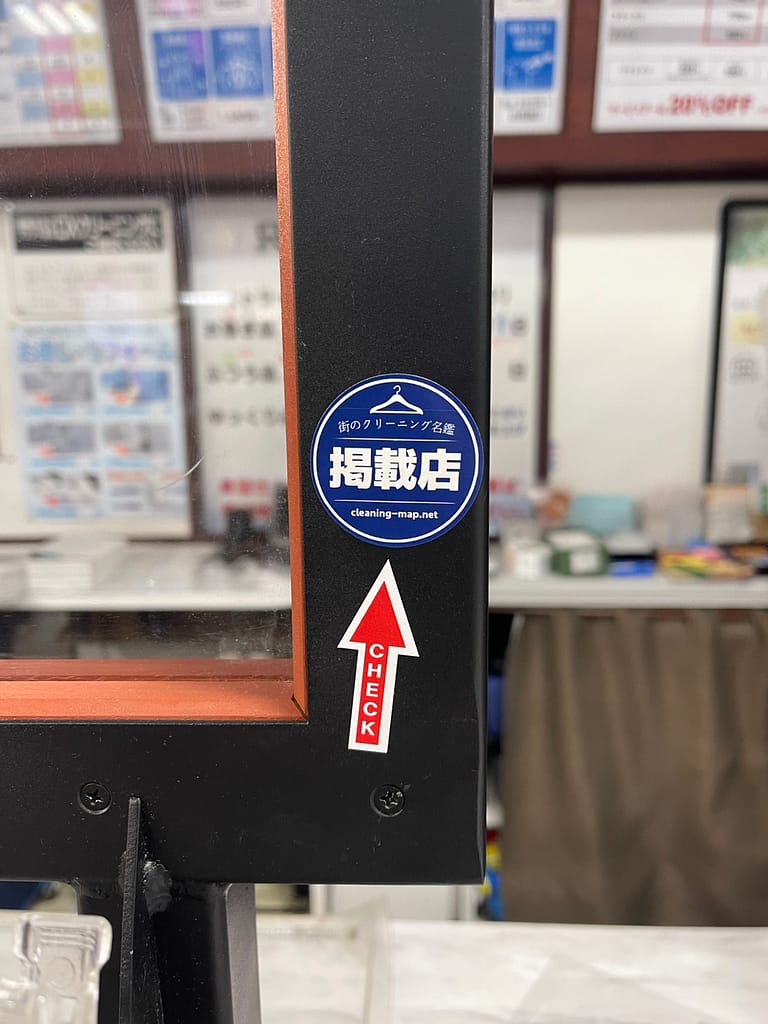 クリーニングうみの店頭ドアに設置された掲載店バッジ(スマホをかざす位置を示す矢印付きNFC導線の実例)